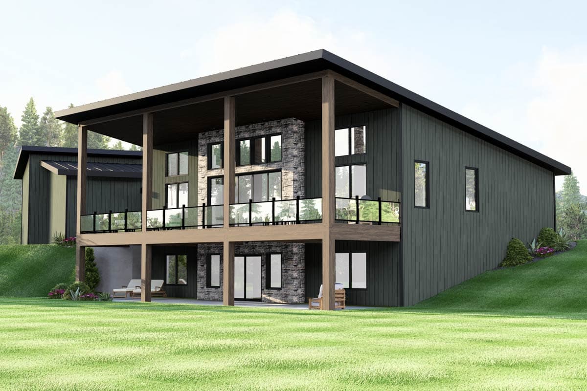 Modern two-story house with a flat roof and stone chimney, featuring a covered deck and large windows overlooking a green lawn.