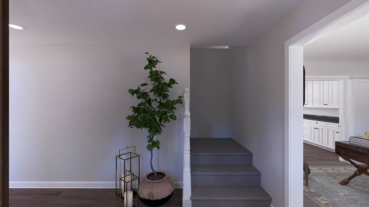 Interior view of a house entrance with stairs to the left, a decorative plant, and a view into a white kitchen.