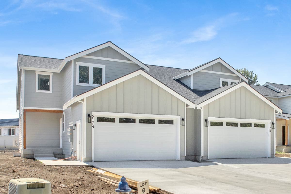 Two-story house plan exterior with overlapping gables, two-car garages, and visible siding.