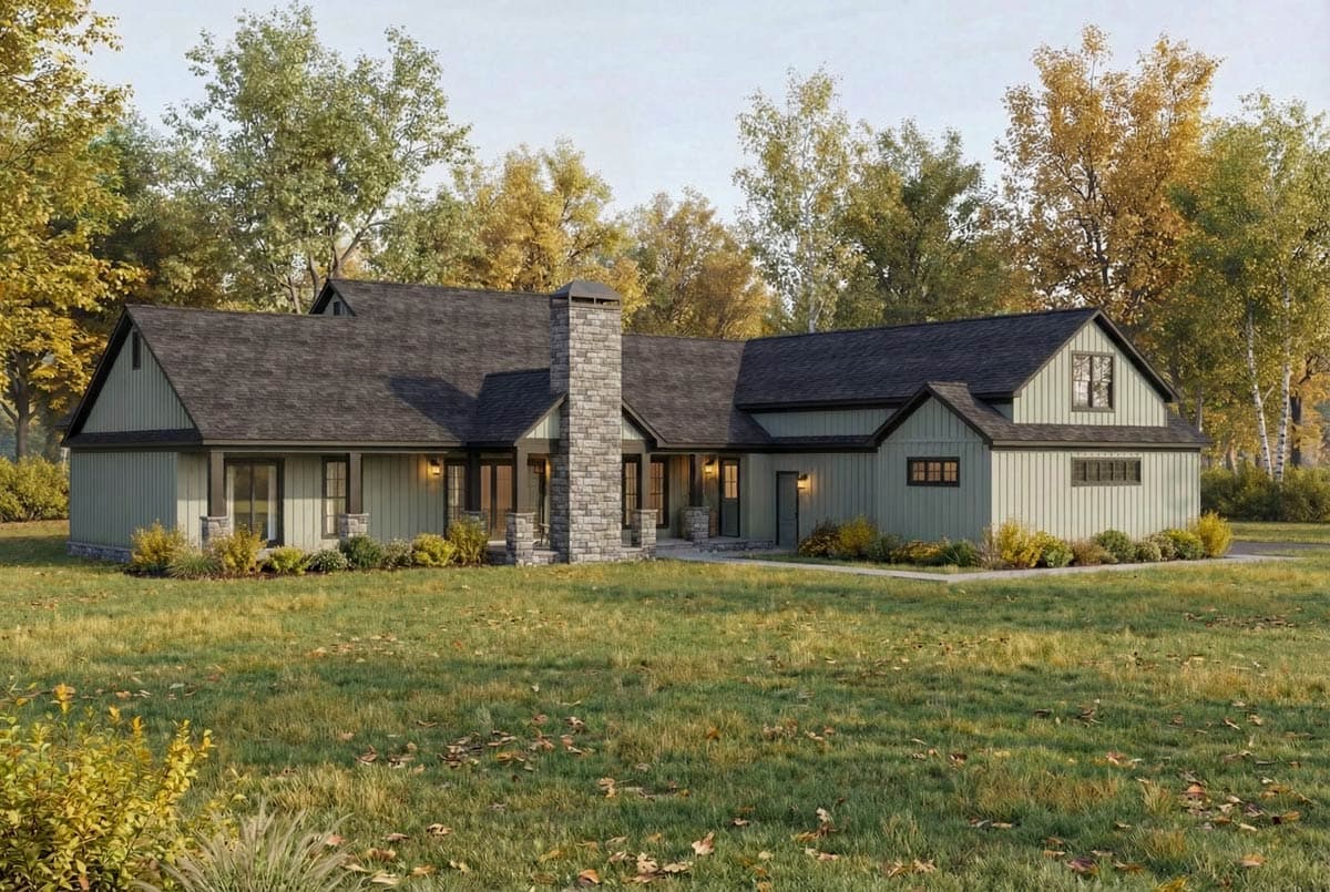 A modern farmhouse with a stone chimney, set in a grassy yard, surrounded by trees with autumn-colored leaves under a bright sky.