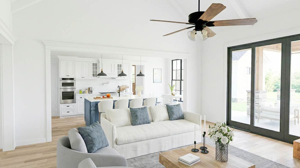 A bright and airy living room with a white sofa, open kitchen, and a ceiling fan. Large glass doors lead to an outdoor patio area.