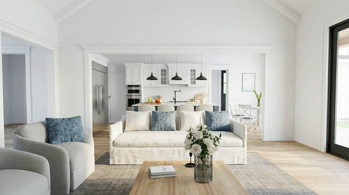 A bright, modern living room with a white sofa, a view into the kitchen, and a wooden coffee table with a vase of flowers.