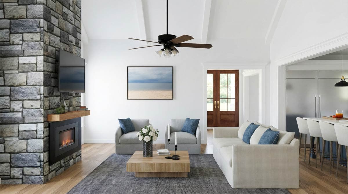 Spacious, modern living room with a stone fireplace, light-colored furniture, and a ceiling fan. Includes a glimpse into an open kitchen area.