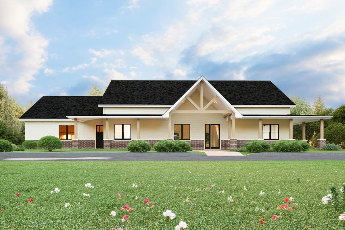 A cream-colored, modern house with a black roof, symmetrical windows, and a covered porch. Lush green grass and flowering bushes in front.
