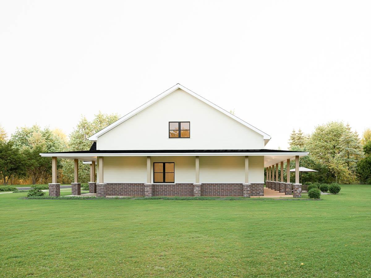House plan exterior. One-story Modern Farmhouse with wrap-around porch, brick foundation, and gabled roof.