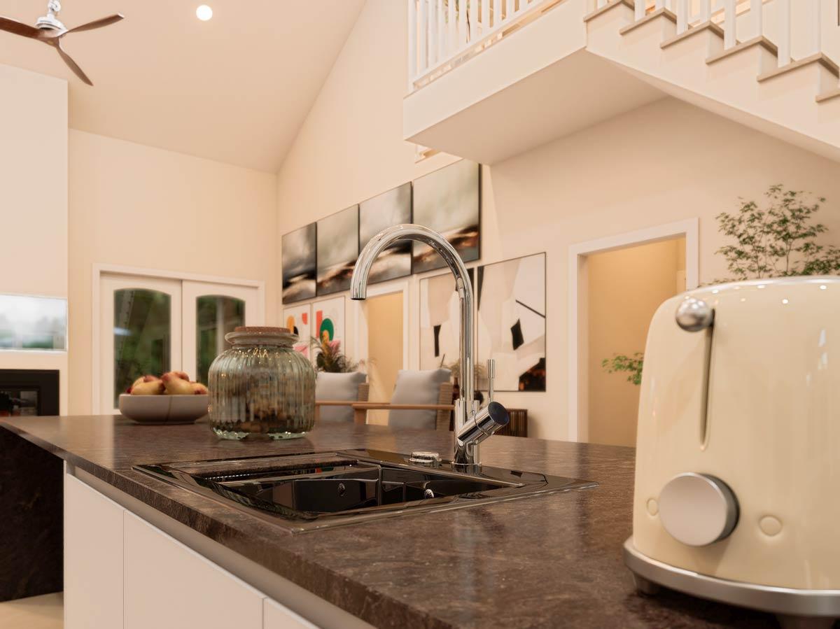 Kitchen island with sink and faucet, vaulted ceiling with fan, staircase above, and abstract art on wall.