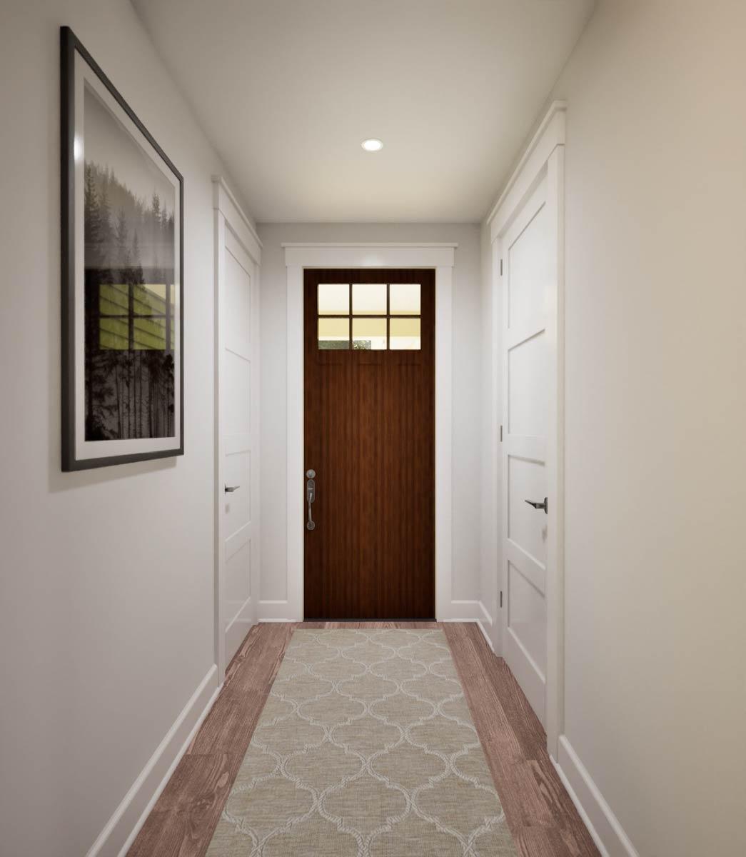 Interior view of a hallway with a dark wood door featuring a nine-pane window, leading to interior rooms. Wood floors and wall art visible.