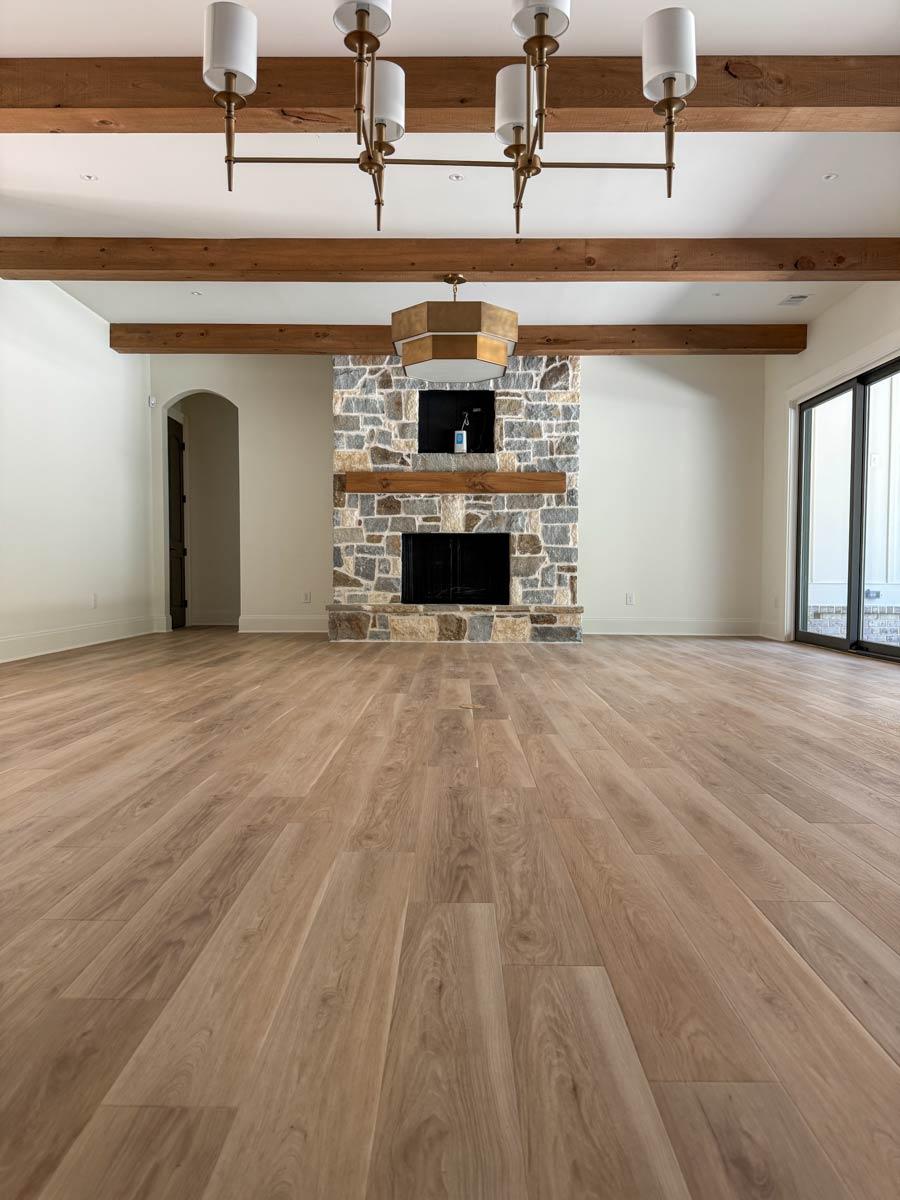 Interior view of living room with stone fireplace, wood beams on ceiling, wood floor, and large glass doors.