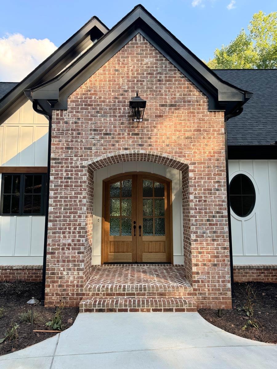 Modern Farmhouse house plan exterior with brick facade, arched entry, double wood doors, and board and batten siding.