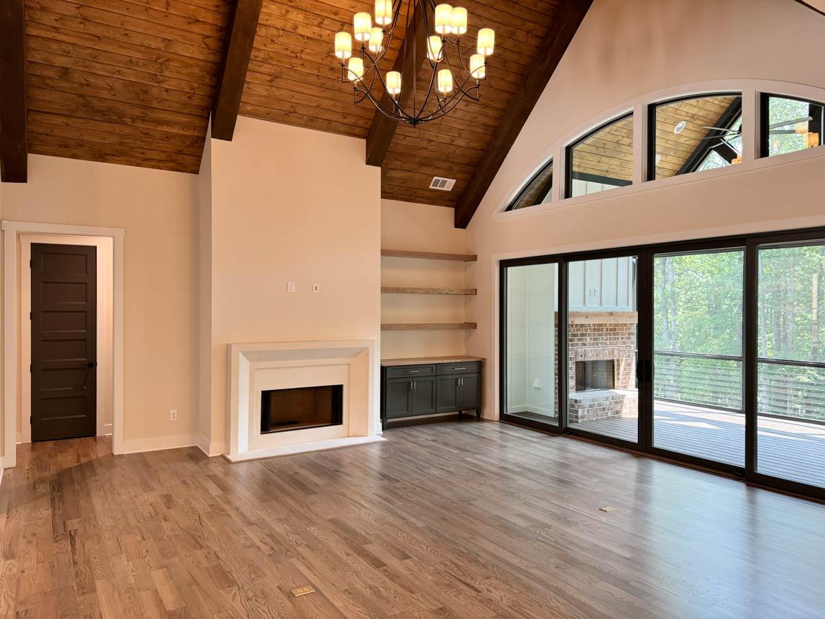 Great room with vaulted wood-beamed ceiling, fireplace, and large sliding glass doors with a view of the deck and trees.