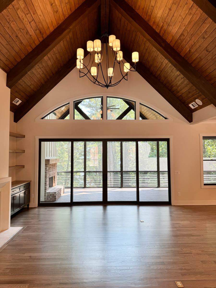 Living room with vaulted wood-beamed ceiling, large windows, sliding glass doors to deck, and brick fireplace.