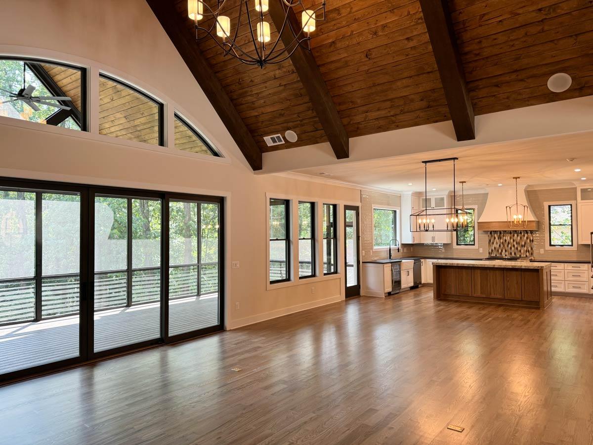 Open concept living space with vaulted wood beam ceiling, large windows, sliding glass doors to deck, and kitchen with island.