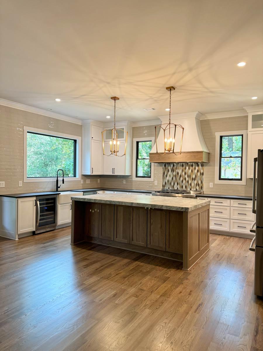Kitchen interior with large island, white cabinets, subway tile backsplash, and modern pendant lights.
