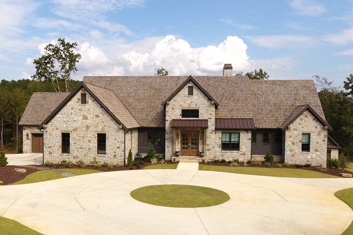 A large stone-clad house with a circular driveway. The roof is wood shingle, and the entrance has double doors under a copper awning.