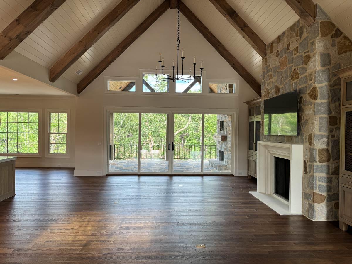 Great room with vaulted beamed ceiling, stone fireplace, large windows, and sliding glass doors leading to an outdoor patio.