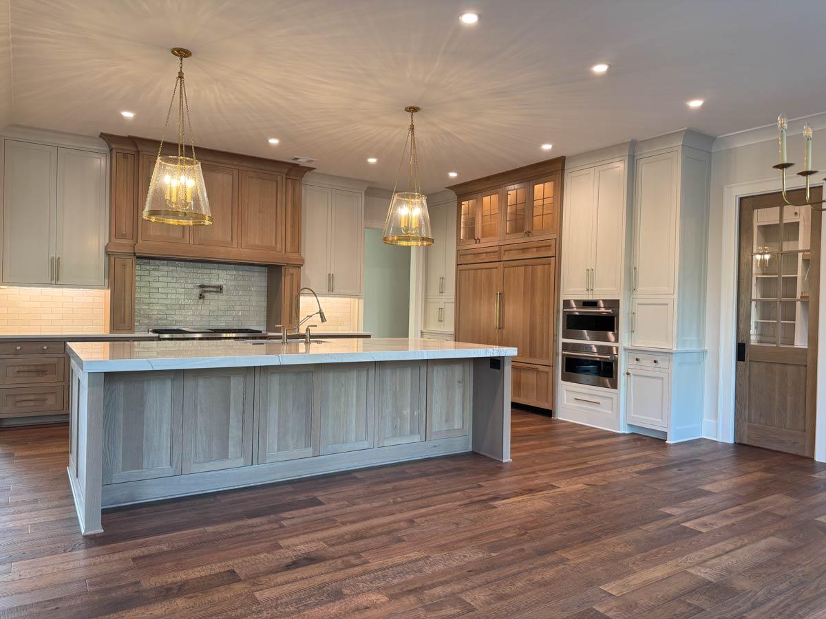 Kitchen with large island, custom wood cabinetry, built-in refrigerator, double ovens, and glass-paneled door.
