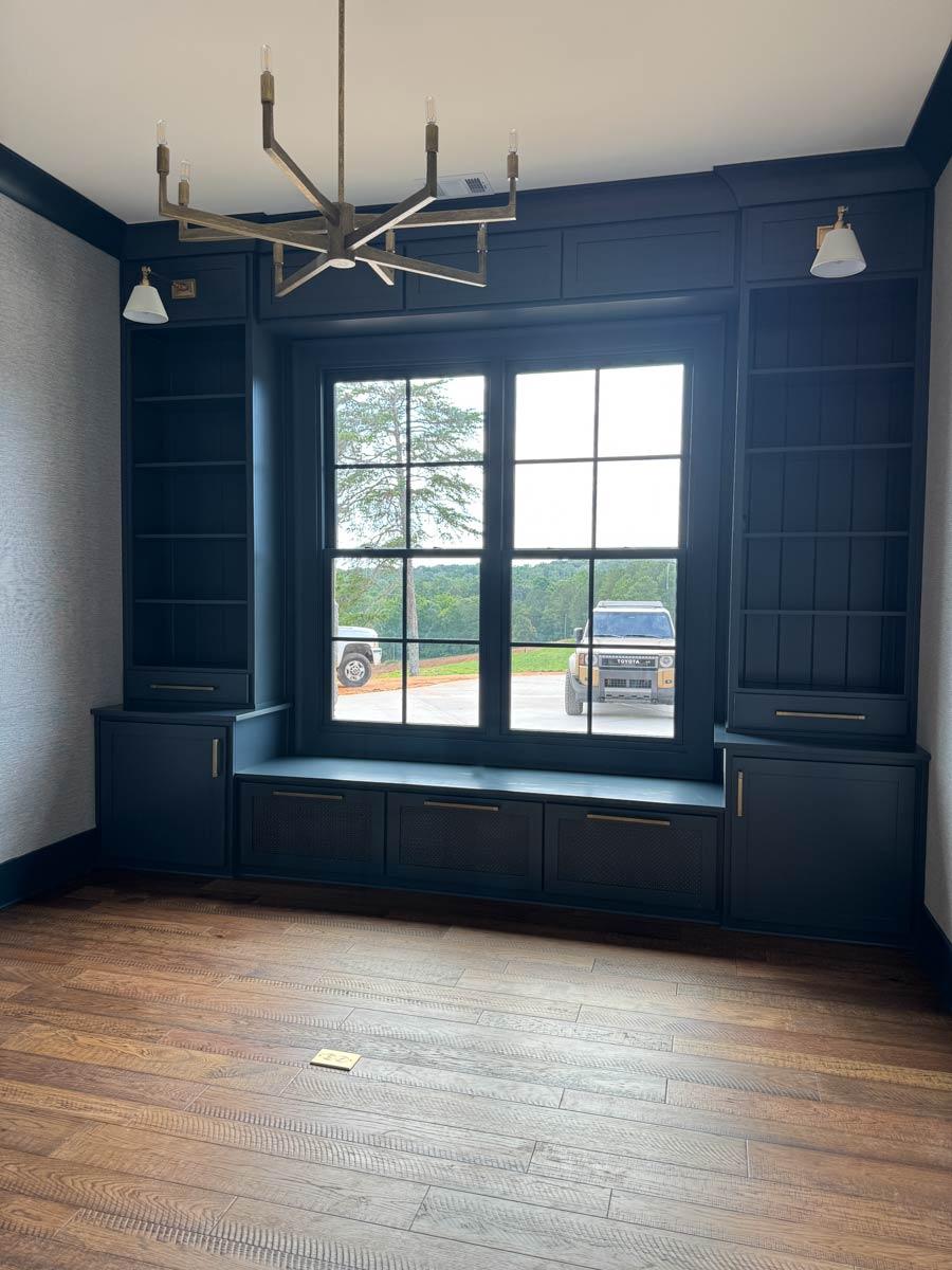 Built-in dark blue cabinetry with shelves, storage, and a window seat surrounds a large multi-pane window.