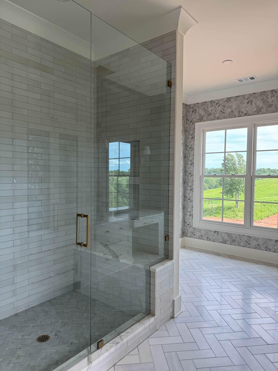 Bathroom interior with glass-enclosed shower with subway tile, marble bench, and herringbone tile floor.