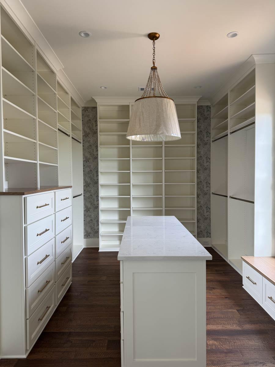 Walk-in closet interior with floor-to-ceiling shelving, central island with stone countertop, and built-in drawers.