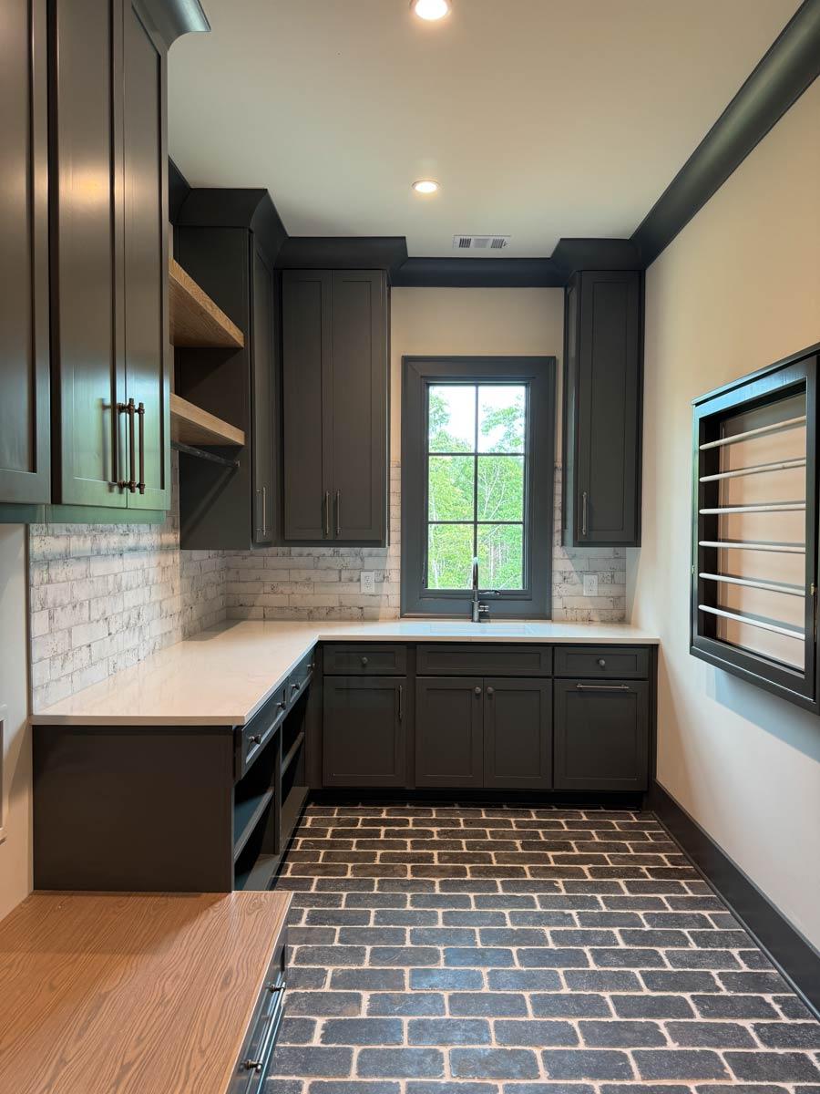 Laundry room with dark cabinets, white brick backsplash, quartz countertop, and dark brick flooring.