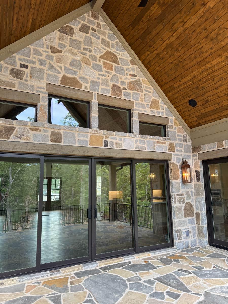 House plan exterior with stone facade, large sliding glass doors, timber-framed gabled roof with wood ceiling, and clerestory windows.