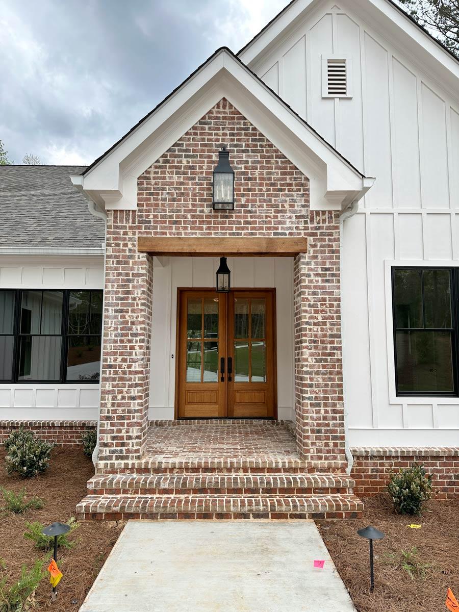 House plan exterior featuring brick facade entrance, double wooden doors, gable rooflines, and board and batten siding.