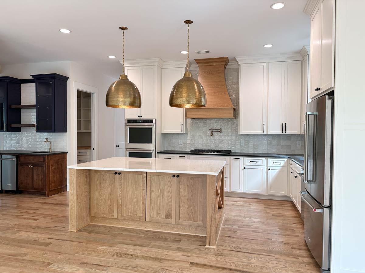 Kitchen with central island, stainless steel appliances, wood range hood, white cabinets, and subway tile backsplash.
