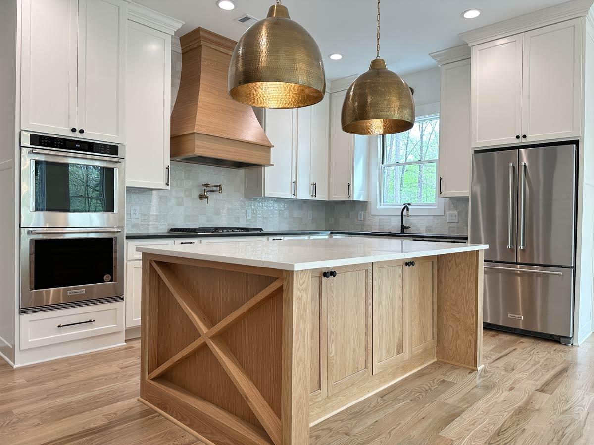 Kitchen with white cabinets, wood island, double ovens, stainless steel refrigerator, and large pendant lights.