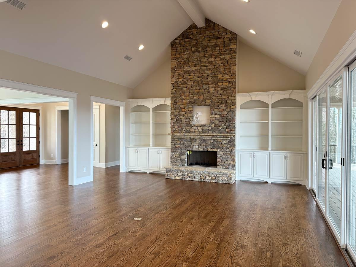 Interior view of great room with vaulted ceiling, stone fireplace, built-in bookshelves, and wood flooring.