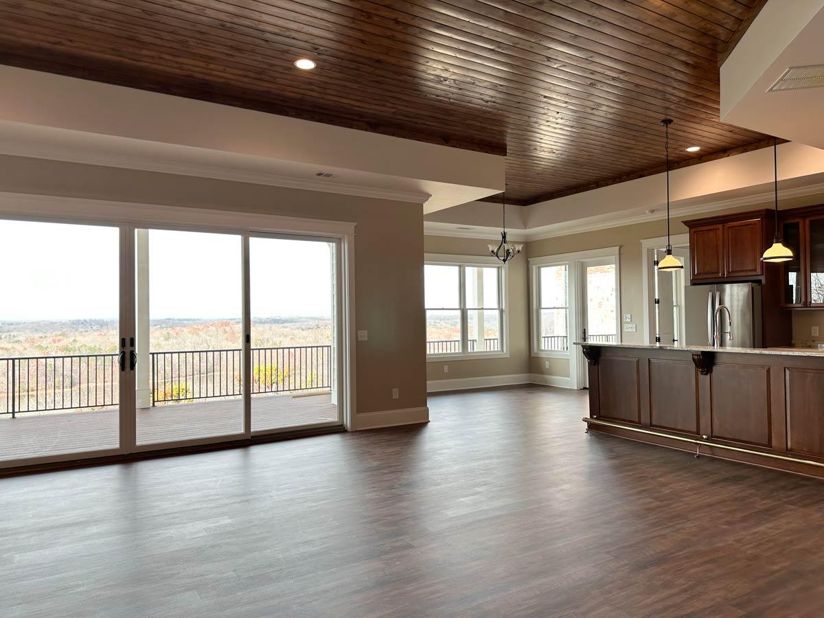 Interior view of living area with a wet bar, wood plank ceiling, and large sliding glass doors opening to a deck with a scenic view.