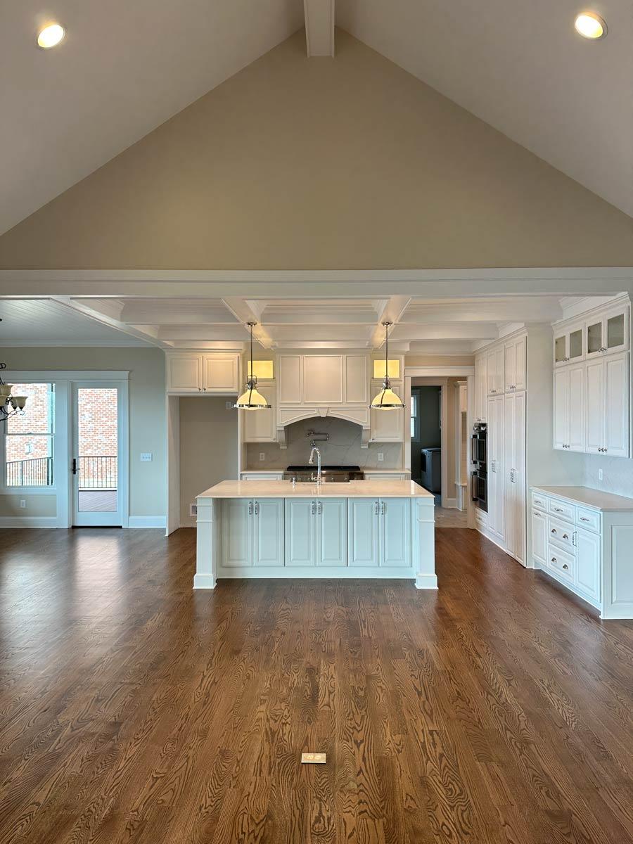 Interior view of a spacious kitchen with a large island, vaulted ceiling with exposed beams, and white cabinetry.