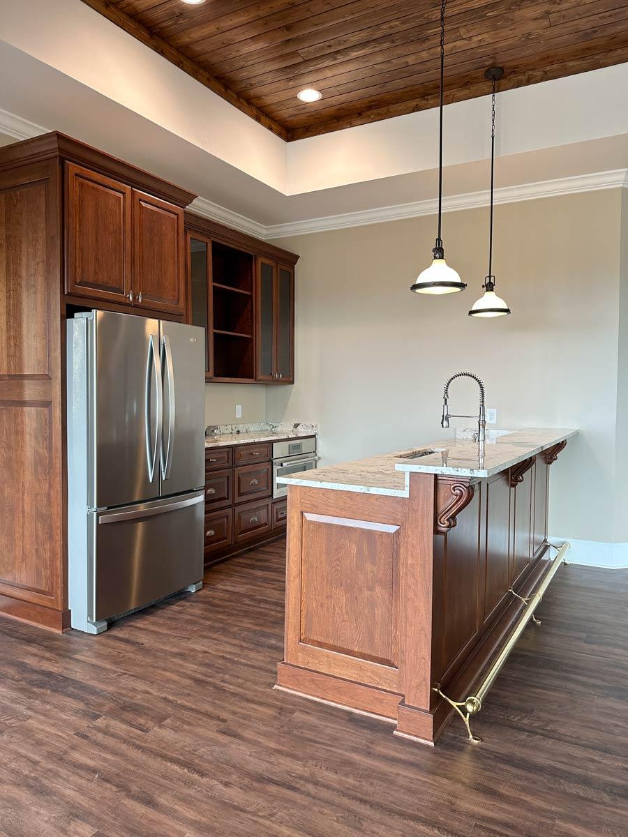 Kitchen area with wood paneled ceiling, stainless steel refrigerator, and large wood island with granite countertop.