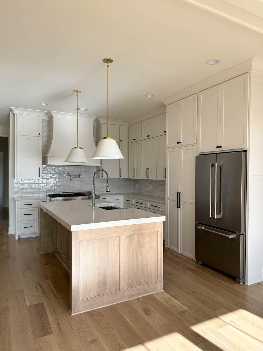 Kitchen with island, white shaker cabinets, subway tile backsplash, gas range, stainless steel refrigerator, and pendant lights.