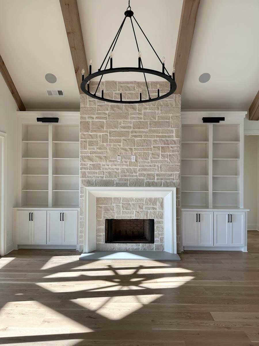 Great room with vaulted ceiling, wood beams, stone fireplace flanked by built-in bookshelves and cabinets.