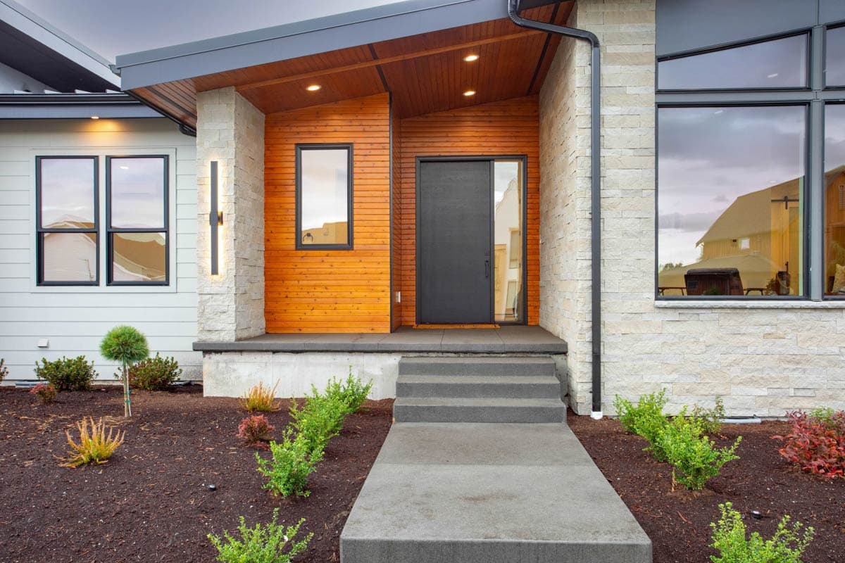 Modern house exterior with wood siding, stone accents, angled roof, and dark metal door.