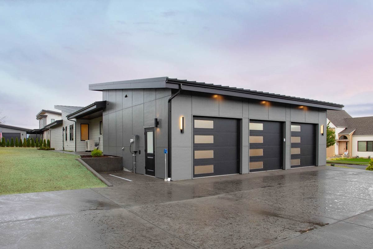 Modern house plan exterior with a three-car garage featuring dark doors with horizontal windows, a gray panel facade, and a low-slope roof.