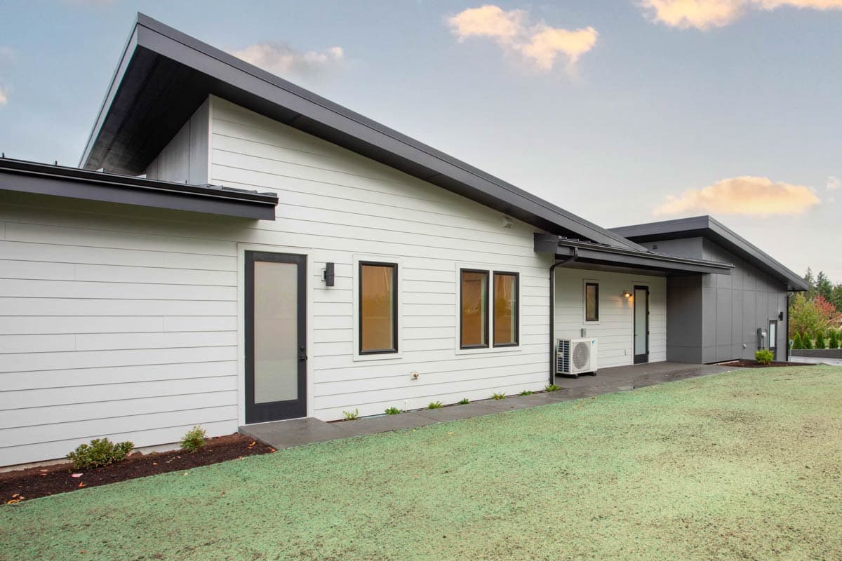 Modern house plan exterior with white horizontal siding, dark pitched rooflines, and multiple windows.