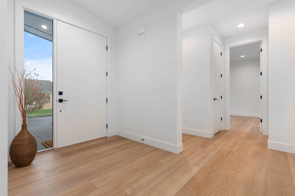 Modern entryway with white flat-panel door, sidelight window, and light wood flooring leading to interior hallway.