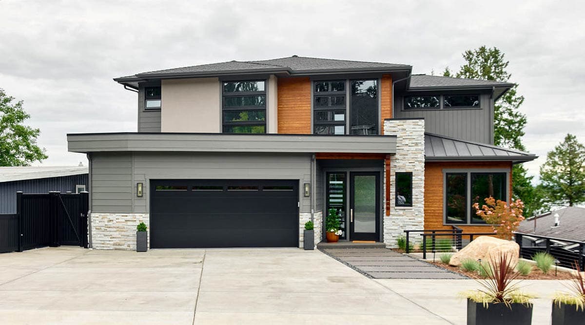 A modern two-story home with a gray exterior, black garage door, and wooden accents. A stone accent column frames the front door.