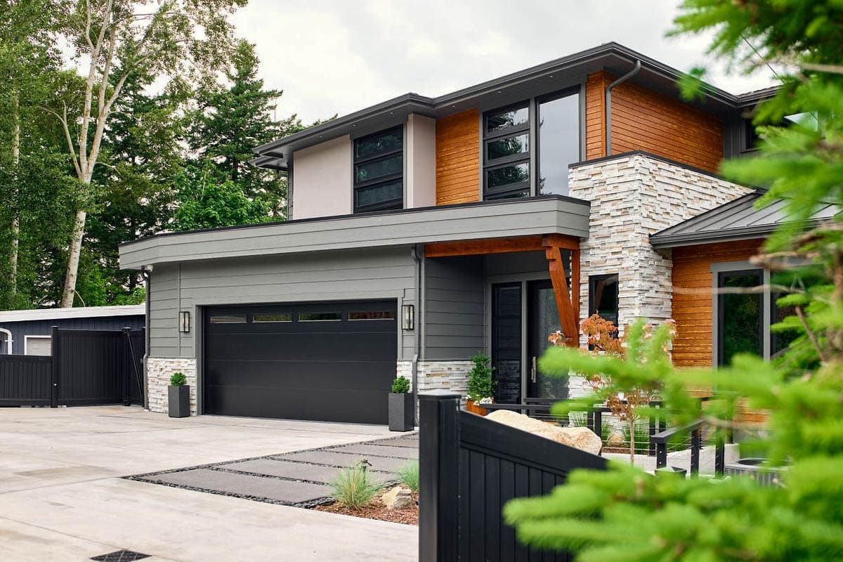 Modern house plan exterior with two stories, a dark garage door, wood siding, stone accents, and multiple windows.