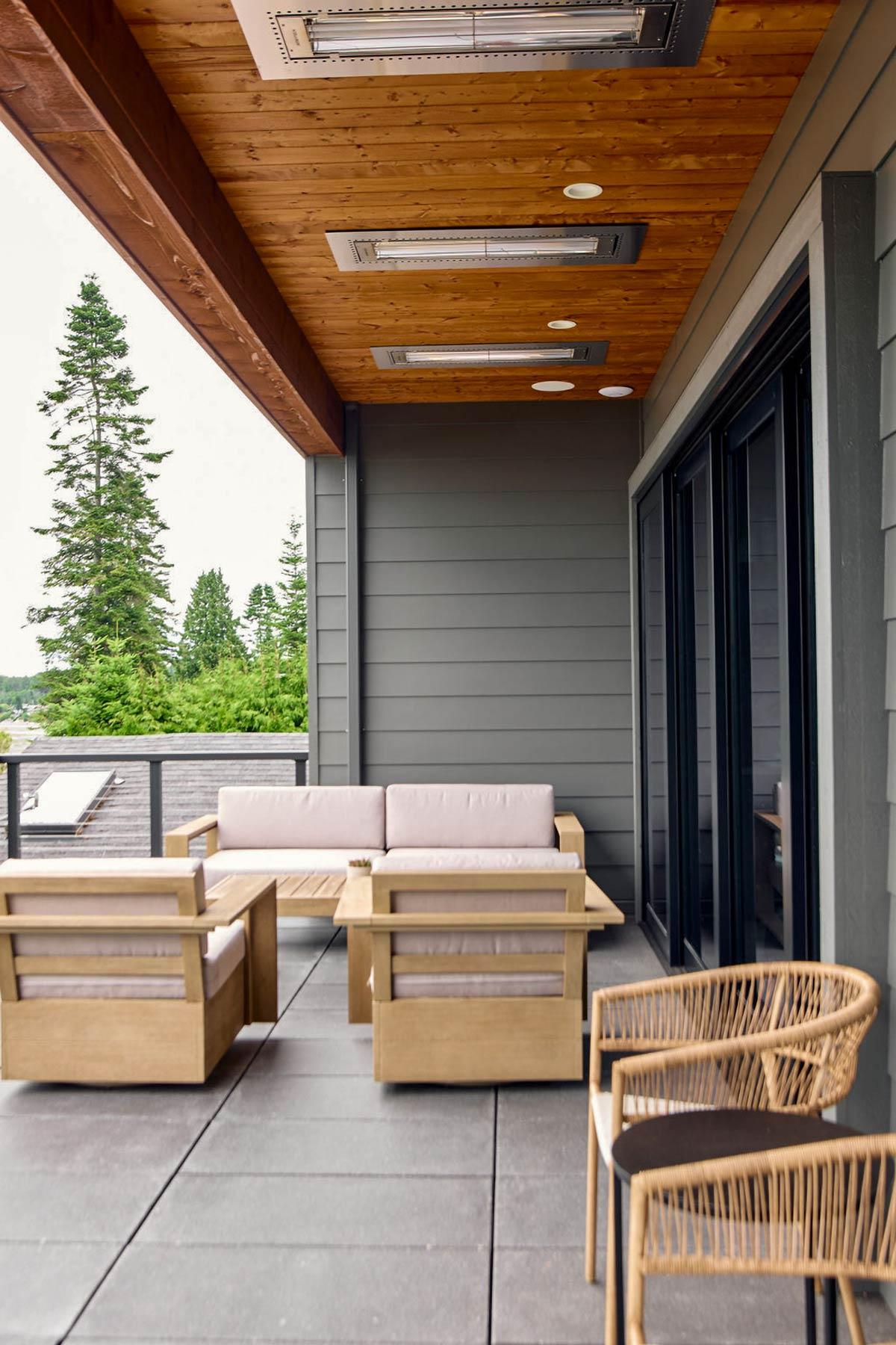 Covered patio with wood ceiling, ceiling heaters, gray siding, and modern outdoor furniture.