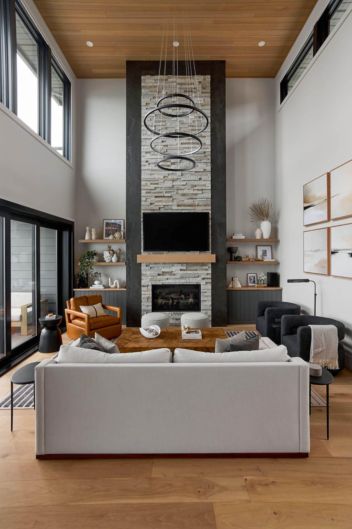 Great room with vaulted wood ceiling, stone fireplace, modern chandelier, and large windows.