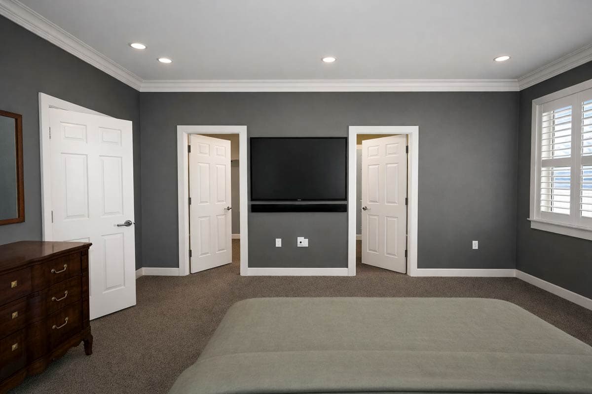 Interior view of a bedroom with a mounted television, two double doors, and a window with shutters.