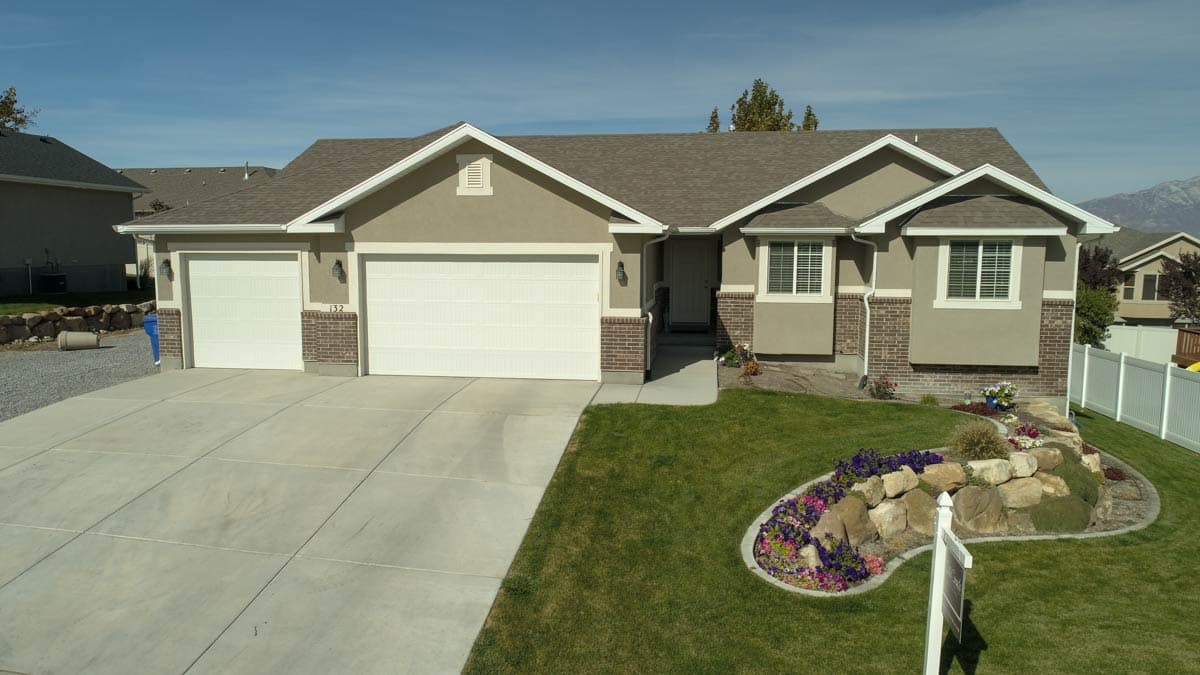 House plan exterior: Ranch style, stucco and brick facade, three-car garage, prominent gables, and covered entry.