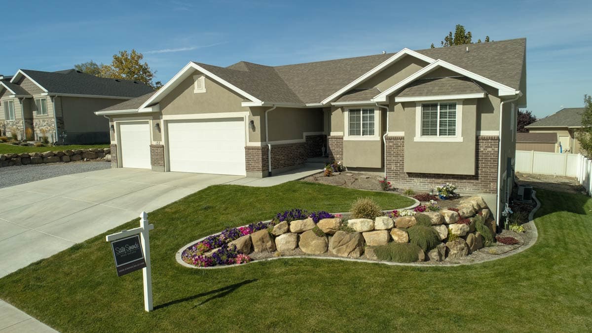 House plan exterior: Ranch style, two-car garage, gabled rooflines, stucco and brick facade, and a tiered rock garden.