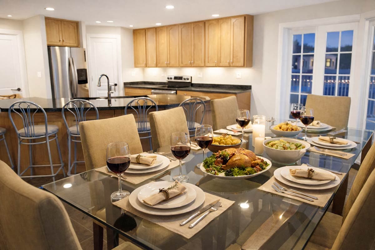Dining room with a glass table set for a meal, adjacent to a kitchen with wood cabinets and island.