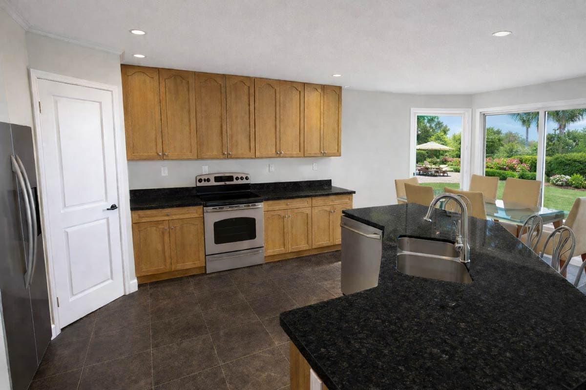 Kitchen with wood cabinets, granite countertops, stainless steel appliances, island sink, and dining area with outdoor view.