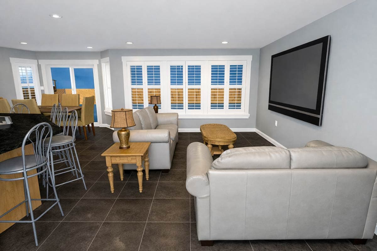 Interior view of a living room with light gray couches, a coffee table, a dining area with bar stools, and large shuttered windows.