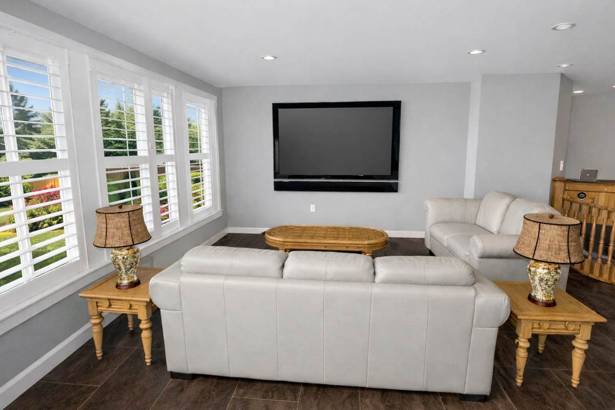 Living room interior with white plantation shutters, leather sofas, wood coffee table, wall-mounted TV, and decorative lamps.