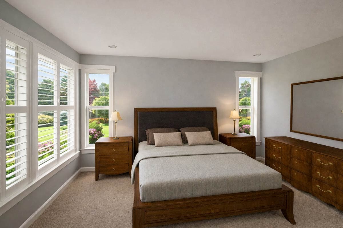 Bedroom with queen bed, nightstands, dresser, and large windows with plantation shutters overlooking a garden.